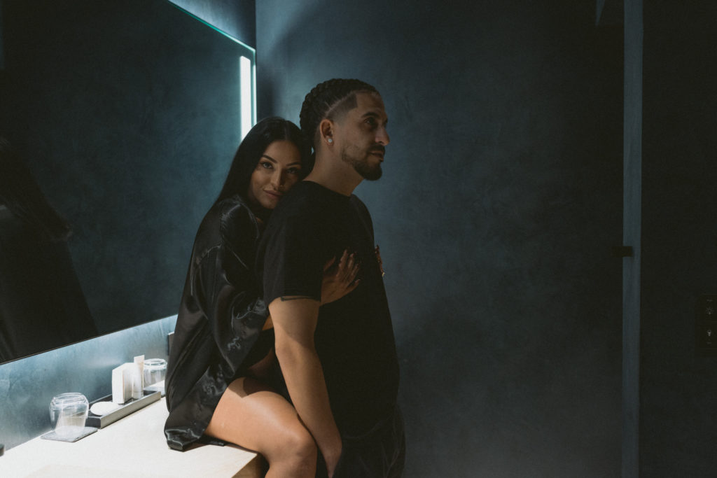 A couple posing for a photo in a moody dark-lit bathroom.
