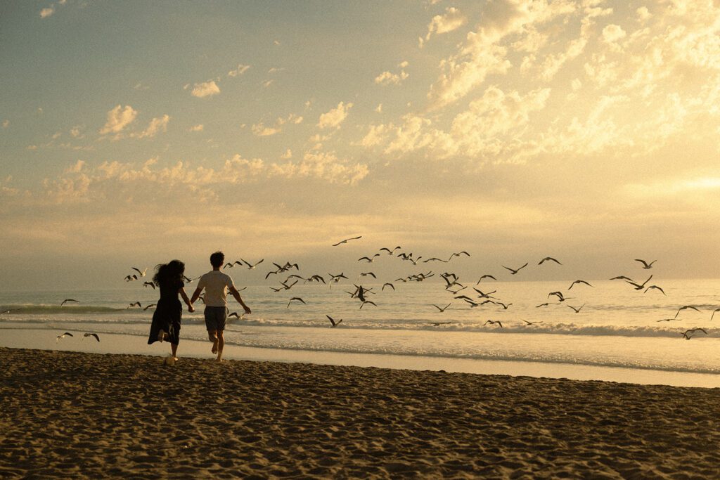 San Diego Anniversary Session with couple running along the sandy beaches into a parade of seagulls