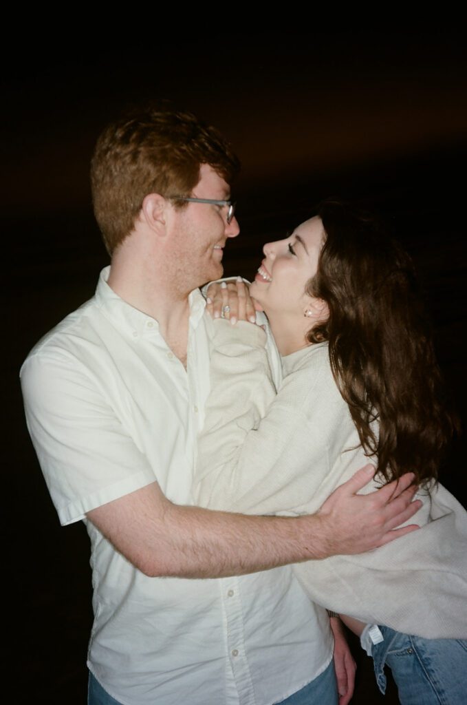 wrapped up in love. couple shares a romantic embrace during their pacific beach pregnancy announcement. cinematic pregnancy photos on film