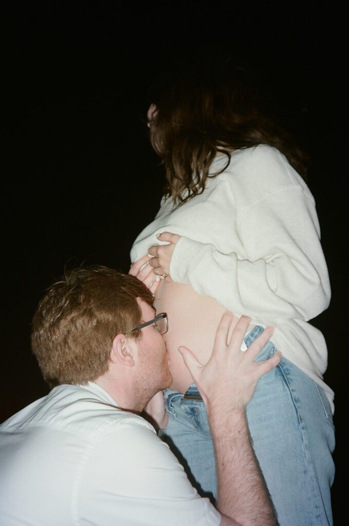 wrapped up in love. couple shares a romantic embrace during their pacific beach pregnancy announcement. cinematic pregnancy photos on film