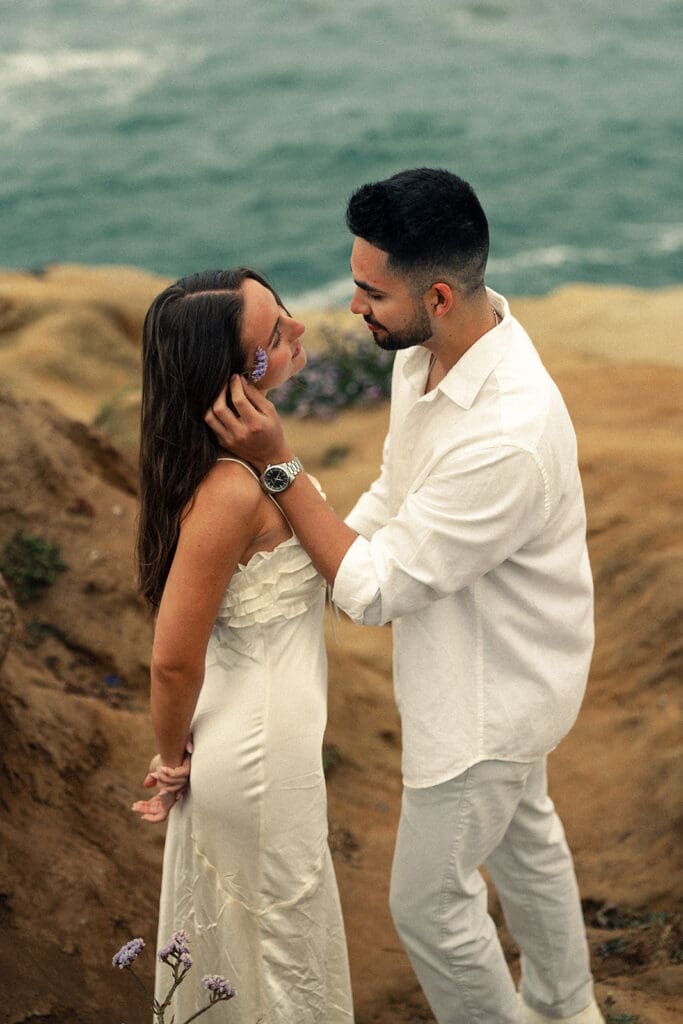 partner placing a purple flower in his fiances hair during their engagement photoshoot